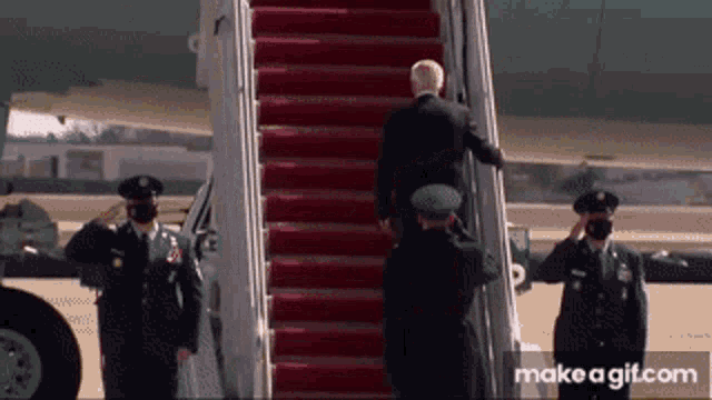 a man in a suit is walking up the stairs of an airplane with make a gif.com in the corner