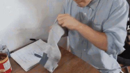 a man in a blue shirt is folding a piece of paper on a table .