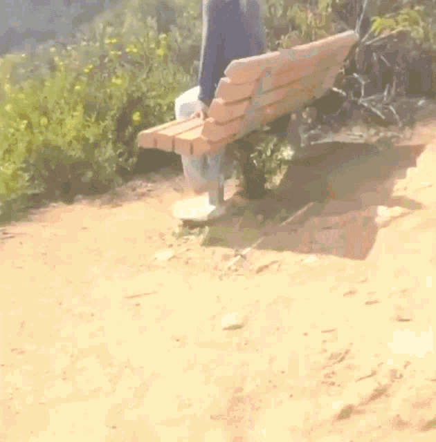 a person is sitting on a wooden bench in the dirt