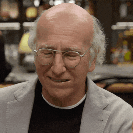 a bald man wearing glasses and a grey jacket smiles