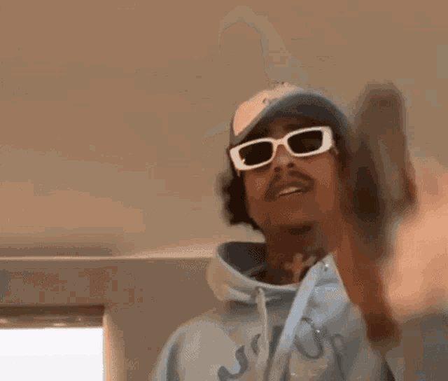 a man wearing sunglasses , a hat and a hoodie is holding a gun .
