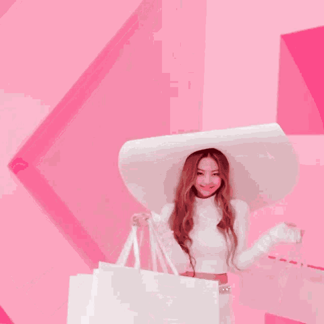 a woman wearing a white hat is holding shopping bags in front of a pink wall