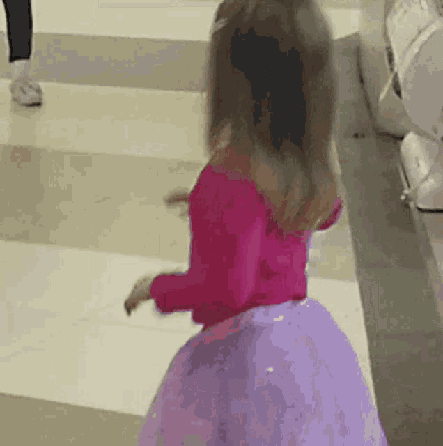 a little girl wearing a pink top and a purple skirt is dancing