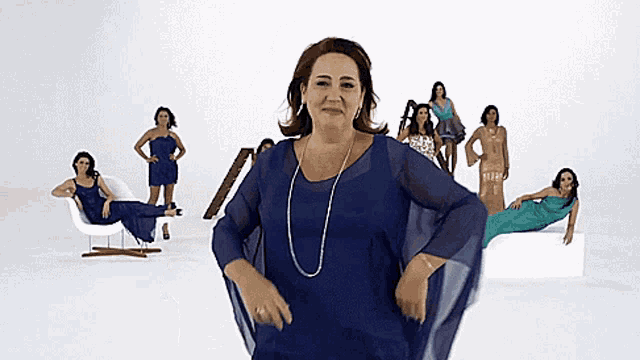 a woman in a blue dress stands in front of a group of women in different dresses