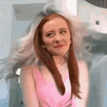 a woman in a pink tank top is making a funny face while her hair is blowing in the wind .