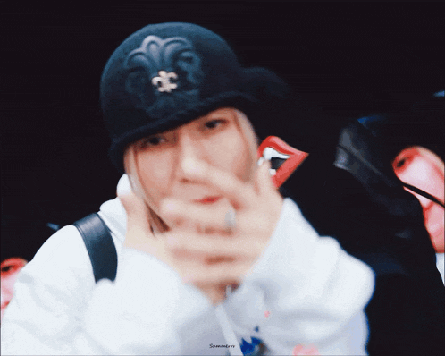 a person wearing a black hat with a fleur de lis on it making a peace sign