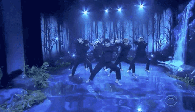 a group of people are dancing in front of a waterfall on a stage
