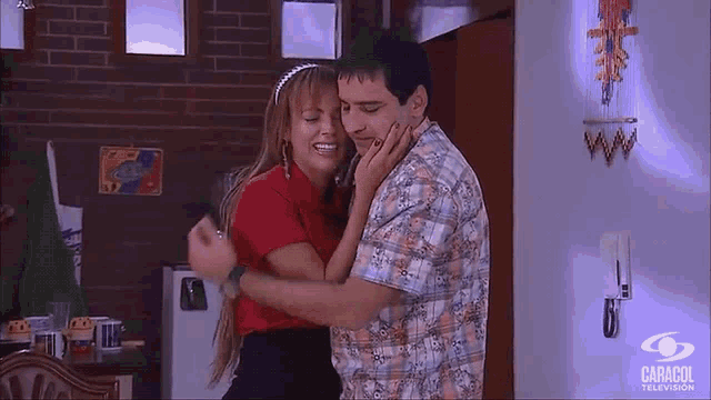 a man and a woman are hugging in a room with a caracol television logo on the wall