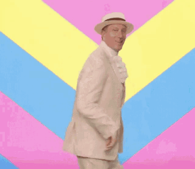 a man in a white suit and hat is dancing against a colorful background .