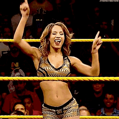 a woman is standing in a wrestling ring with her arms in the air and giving the middle finger .