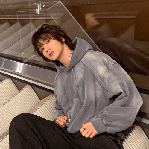 a young man wearing a grey hoodie sits on an escalator