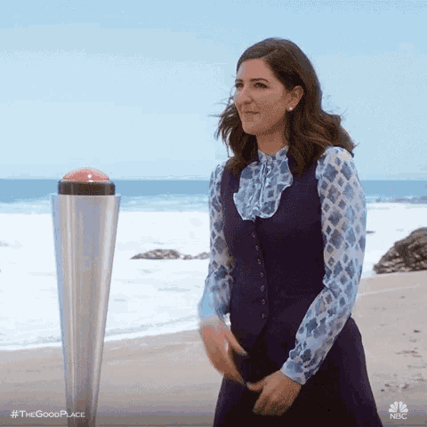 a woman in a purple dress is standing on a beach next to a pole with a red button on it .