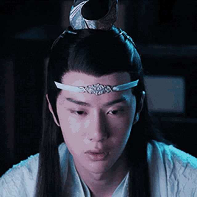 a young man with long hair and a headband on his head is looking down .