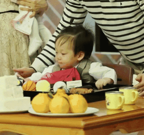 a little boy is sitting at a table with a tray of lemons and cups on it .