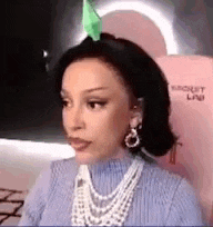 a woman wearing a pearl necklace and earrings is sitting in a chair with a green flower on her head .