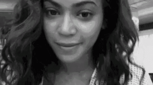 a black and white photo of a woman with long curly hair making a funny face .