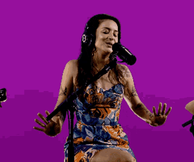 a woman wearing headphones singing into a microphone on a purple background