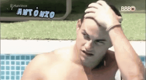 a shirtless man is standing next to a swimming pool holding his head .