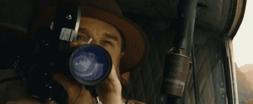 a man in a hat is looking through a red camera