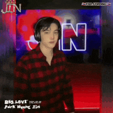 a man wearing headphones and a plaid shirt is standing in front of a sign that says big love