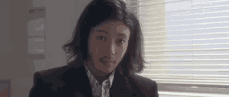 a man with long hair and a beard is sitting in front of a window in a room .