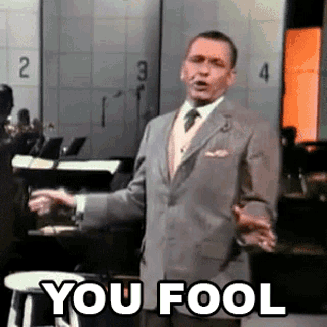 a man in a suit and tie is standing in front of a stool with the words you fool written on it