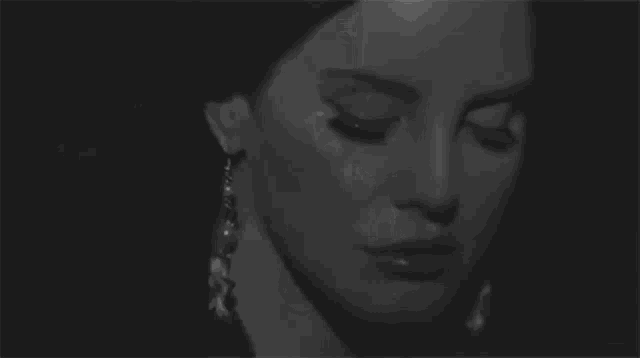 a black and white photo of a woman 's face with her eyes closed and earrings .
