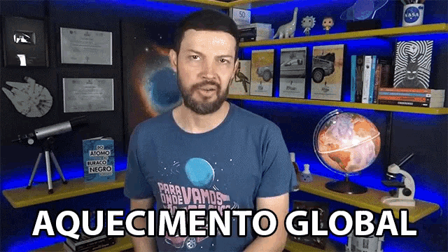 a man with a beard is standing in front of a bookshelf and says aquecimento global