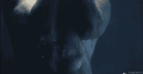 a man without a shirt is taking a shower in a dark room .