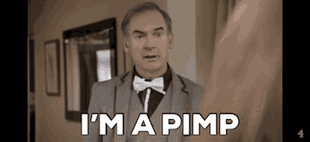 a man in a suit and bow tie is standing in a hallway and says `` i 'm a pimp '' .
