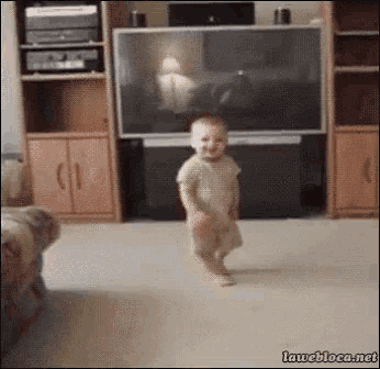 a baby is walking in front of a television in a living room .
