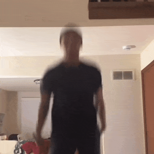 a blurry picture of a man in a black shirt standing in a living room .