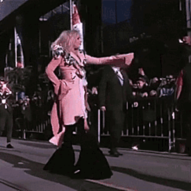 a woman in a pink coat and black pants is walking down a street .