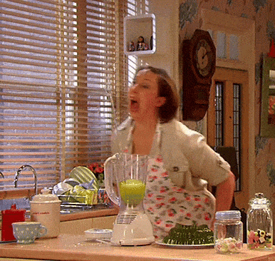 a woman in an apron is making a green drink in a blender in a kitchen
