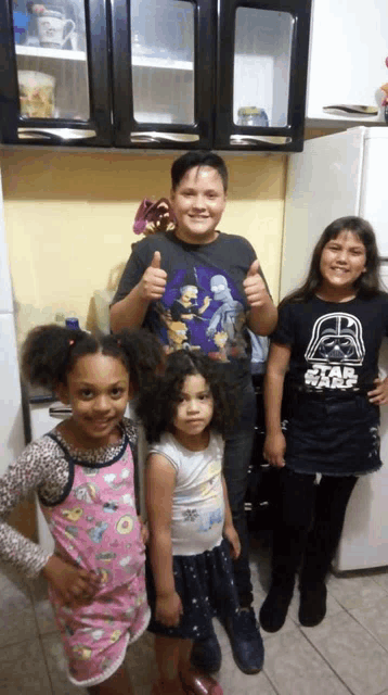a boy wearing a star wars shirt gives a thumbs up with two girls