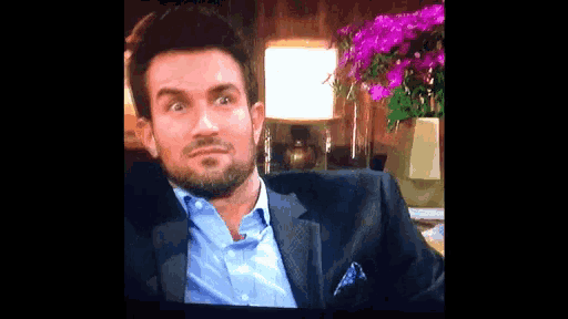 a man in a suit and blue shirt is sitting in front of a table with purple flowers .