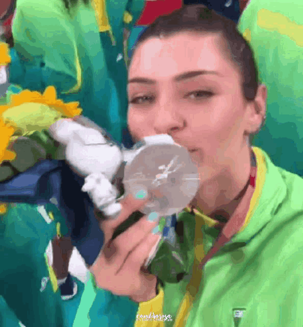 a woman in a green jacket is holding a medal in her mouth
