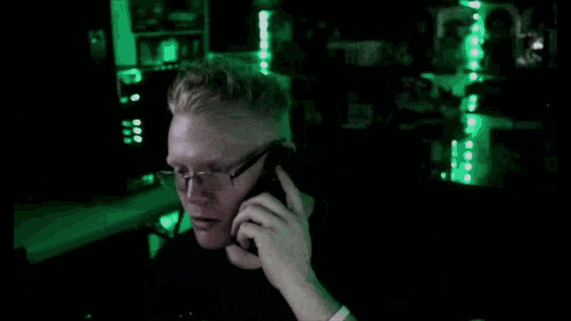 a man wearing glasses is talking on a phone in a dark room