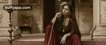 a woman in a red dress is smoking a hookah while sitting on the steps of a building .