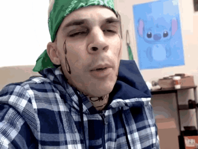 a man wearing a plaid shirt and a green bandana looks at the camera