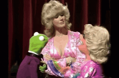 a woman in a pink dress is being held by a kermit the frog