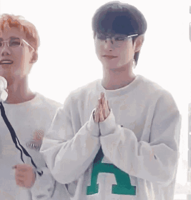 a man wearing glasses and a white sweatshirt is standing next to another man .