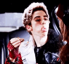 a young man in a leather jacket is eating a piece of food .
