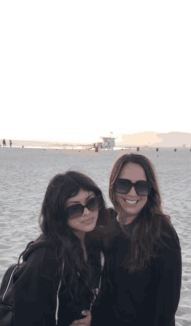 two women wearing sunglasses are posing for a picture on a beach