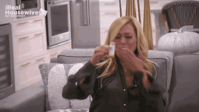 a woman is sitting on a couch with a bottle in her hand and the words real housewives out of context behind her