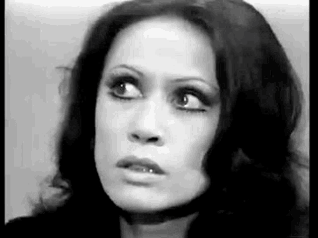 a black and white photo of a woman with long dark hair looking at the camera .