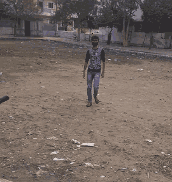 a man wearing a mask walks in a dirt field