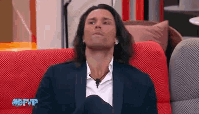 a man in a suit is sitting on a red couch with his eyes closed .