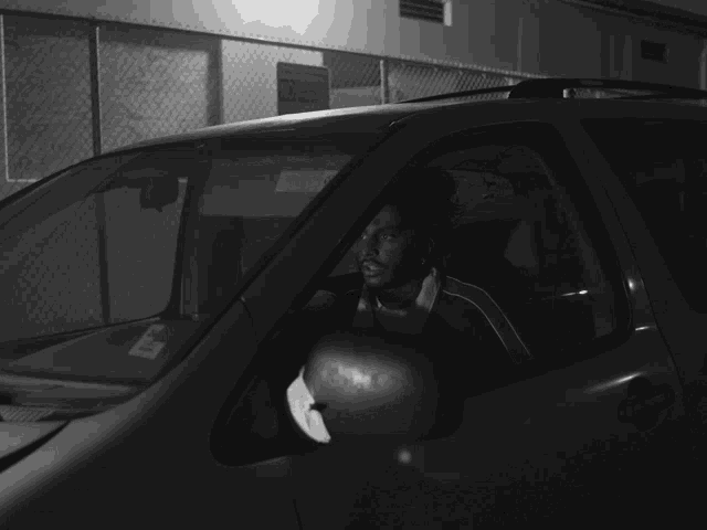 a black and white photo of a man in a car with a parking sticker on the windshield