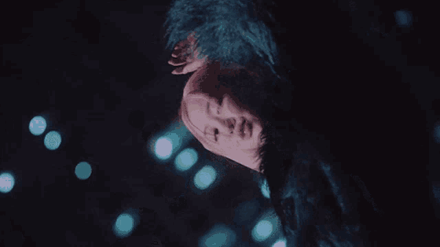 a woman with pink hair and a black fur coat is laying down in the dark .